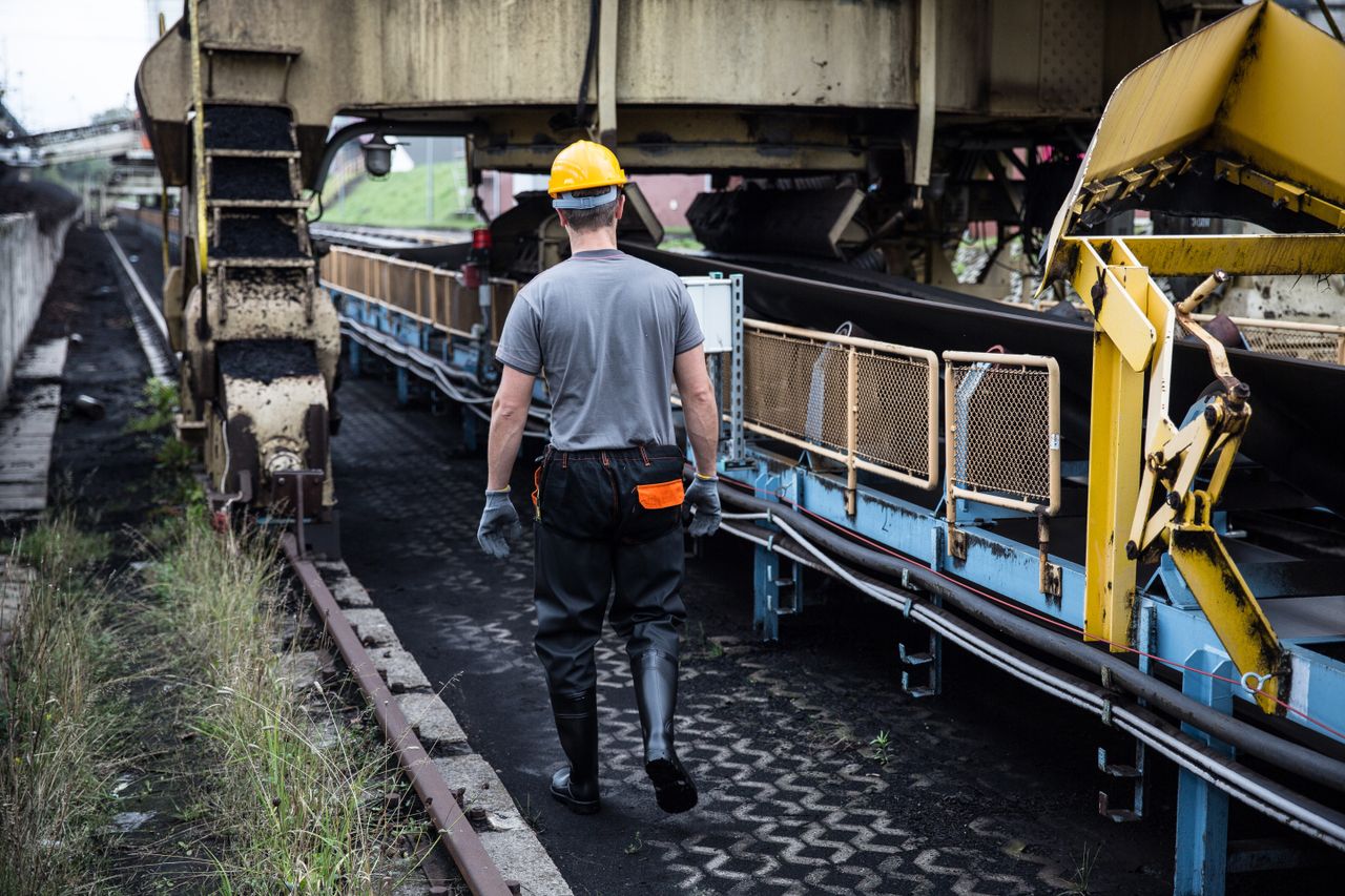 About A worker in safety gear examines industrial machinery in an outdoor setting, showcasing industry work.