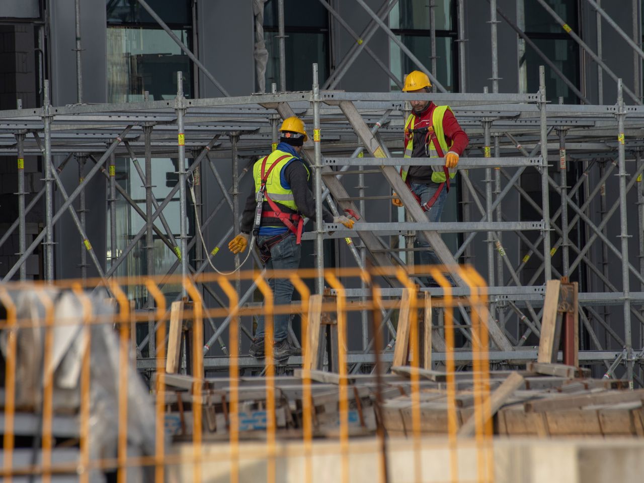 Services Two construction workers wearing safety gear and helmets working on scaffolding outdoors.